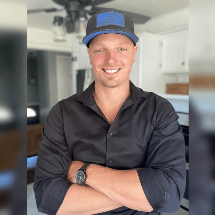 BPC157 Image 6 Smiling man wearing a black button-up shirt and a black-and-blue hat, with a blurred background